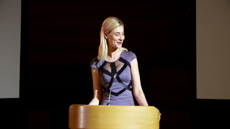 Young-blonde-Caucasian-businesswoman-speaking-in-business-seminar-at-auditorium-4k