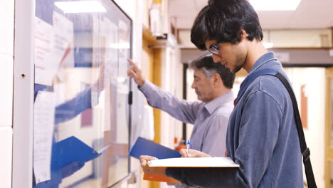 Student-and-teacher-checking-papers-hanging-in-the-hallway