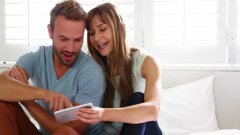 Glückliches-Paar-Sitzt-Auf-Dem-Bett-Und-Benutzt-Ein-Smartphone