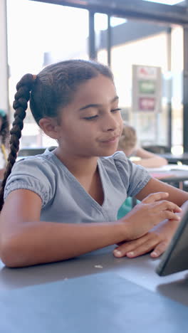Vertical-video:-In-school,-young-girl-with-a-braid-focusing-on-a-tablet