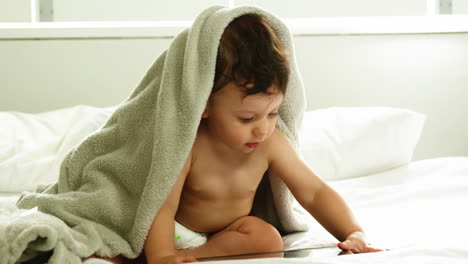 Cute-baby-with-blanket-on-head-playing-with-tablet-
