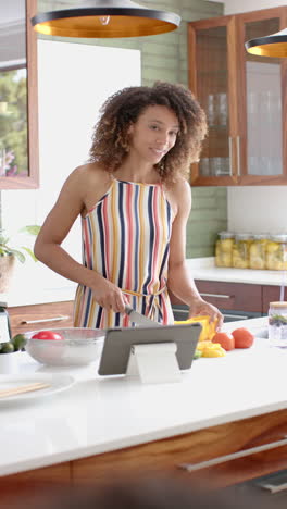 Vídeo-Vertical:-Una-Mujer-Joven-Con-Cabello-Rizado-Usa-Una-Tableta-En-La-Cocina