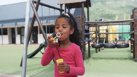 In-a-school-playground,-a-young-biracial-girl-is-blowing-bubbles