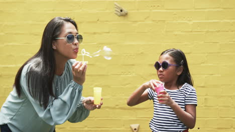Biracial-mother-and-daughter-in-sunglasses-blowing-bubbles