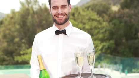 Smiling-waiter-holding-champagne-bottle-and-flute-