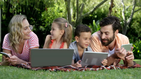 Portrait-of-cute-family-are-lying-on-the-grass-and-using-electronic-devices