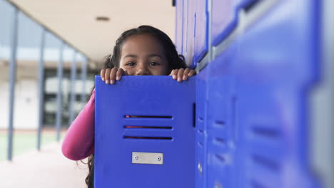In-a-school-hallway,-a-young-biracial-girl-peeks-from-behind-a-blue-locker