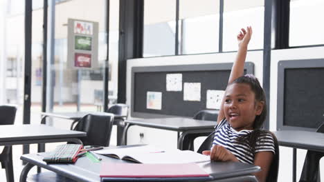 In-a-school-classroom,-a-young-African-American-girl-raises-her-hand-eagerly-with-copy-space