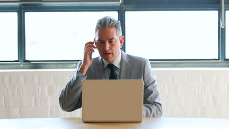 Businessman-using-laptop-and-receiving-a-phone-call