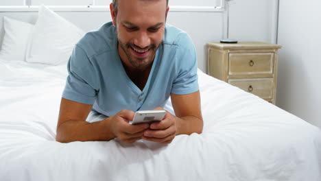 Happy-man-lying-on-bed-using-his-smartphone-