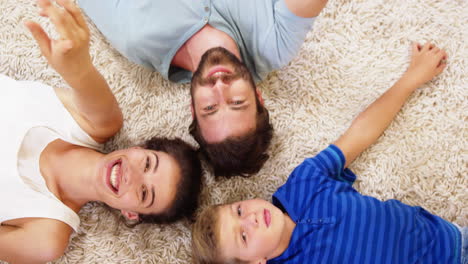 Familia-Feliz-Tumbada-En-La-Alfombra-Y-Apuntando-La-Cámara