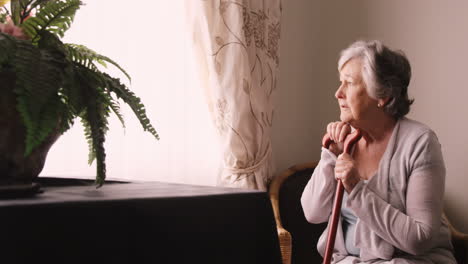 Thoughtful-senior-woman-looking-through-window