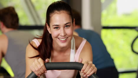 Fit-woman-doing-exercise-bike-smiling-to-the-camera
