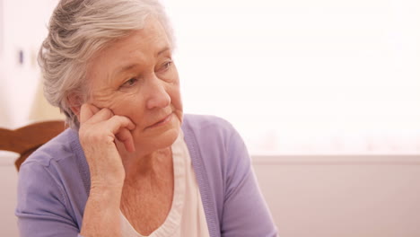 Thoughtful-senior-woman-sitting-at-home