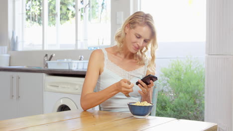 Frau-Isst-Müsli-Und-Schaut-Dabei-Auf-Ihr-Smartphone