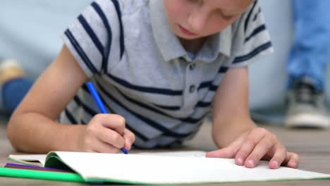 Close-up-on-a-boy-lying-on-a-floor-and-doing-colouring-pictures