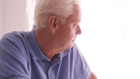 Thoughtful-senior-man-looking-through-window