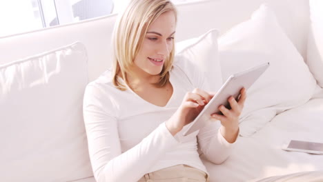 Blonde-woman-smiling-and-using-tablet-on-a-sofa