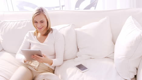 Blonde-woman-smiling-and-using-tablet-on-a-sofa
