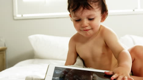 A-baby-boy-is-looking-his-tablet-on-the-bed