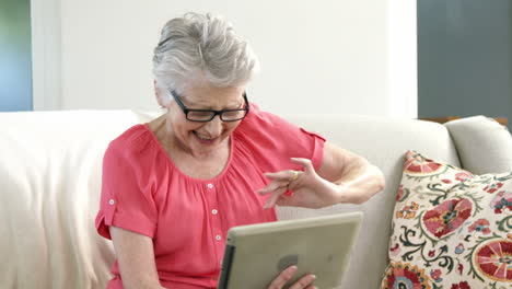 -Ältere-Frau-Mit-Digitalem-Tablet-Im-Wohnzimmer