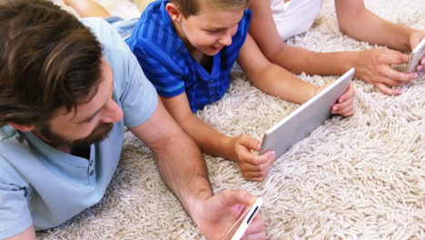 Familia-Feliz-Usando-Tableta-Y-Teléfono-Inteligente-Tumbado-En-Una-Alfombra