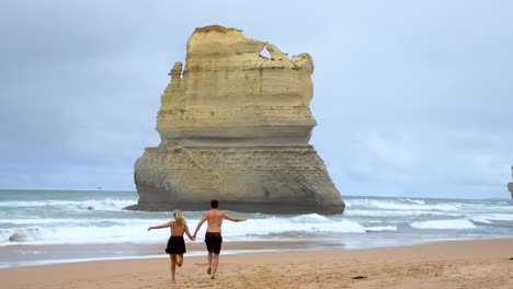 Camera-video-of-a-couple-running-on-the-beach-at-the-bottom-of-Gibson-steps-near-the-12-Apostles-along-the-Great-Ocean-Road-in-Victoria,-Australia