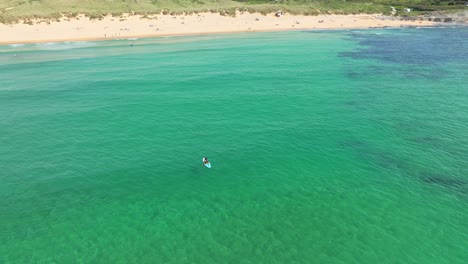 Isolated-Paddle-Boarder-Paddles-Back-to-Constantine-Bay-in-Cornwall-with-an-Aerial-Drone-Orbiting-the-Individual,-UK
