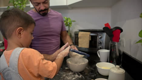 Slow-motion-of-a-mexican-latin-small-boy-wearing-denim-overalls-sifting-flour-with-his-father-making-cookies-in-the-kitchen