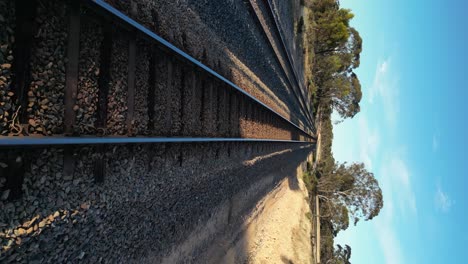Drone-flying-at-low-altitude-over-train-rails-in-rural-landscape