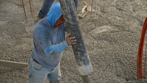 Close-up-of-a-mexican-latin-construction-worker-with-a-hoodie-applying-fresh-concrete-with-a-boom-pump-in-slow-motion