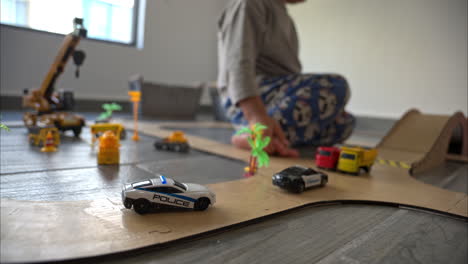 Toma-De-Enfoque-Selectivo-En-Cámara-Lenta-De-Un-Niño-Pequeño-Jugando-Con-Los-Juguetes-De-Su-Auto-Y-Su-Madre-En-Una-Pista-De-Cartón-Casera-En-Su-Habitación