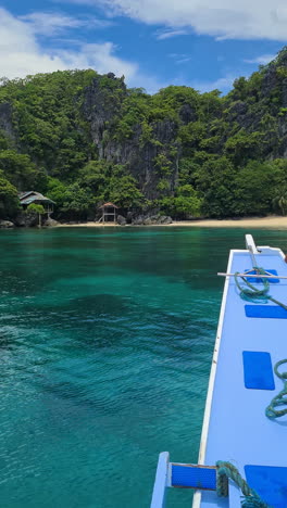 Vertical-Video,-Arriving-With-Boat-on-Empty-Beach-Under-Limestone-Cliff-With-Abandoned-House,-El-Nido,-Philippines