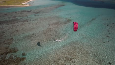 Kitesurfer-gliding-on-crystal-clear-turquoise-waters,-aerial-view