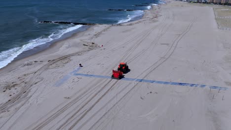 An-aerial-view-of-an-orange-tractor-raking-an-empty-beach-on-a-sunny-day