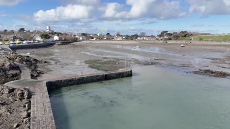 Fast-Reveal-of-Bordeaux-Harbour-Guernsey-at-low-tide-with-harbour-wall,jetty,-boats-drying-out-on-sand,beach-and-cottages-in-the-background-on-a-bright-day