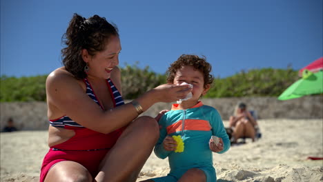 Zeitlupe-Einer-Mexikanischen-Lateinamerikanischen-Mutter-Im-Badeanzug,-Die-Am-Strand-In-Mexiko-Die-Nase-Ihres-Sohns-Mit-Seidenpapier-Putzt