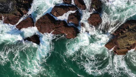 Schaumige-Wellen-Plätschern-Auf-Riesigen-Felsen-Des-Strandes---Luftaufnahme-Von-Oben-Nach-Unten