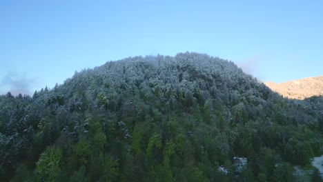 Snow-capped-forested-hill-under-a-clear-sky,-marking-a-seasonal-transition-from-winter-to-spring