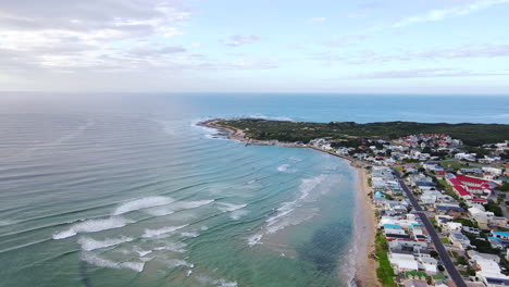 Vista-Aérea-Sobre-El-Océano-De-La-Bahía-Costera-Al-Oeste-Con-El-Puerto-Al-Lado