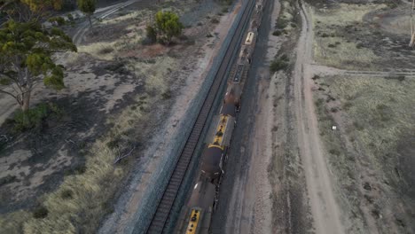 Drone-flying-over-fuel-cargo-train-passing-in-rural-landscape,-Western-Australia