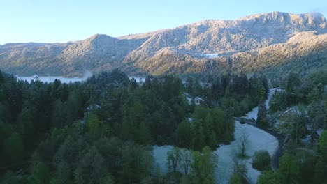 Una-Vista-Impresionante-De-La-Montaña-Cubierta-De-Nieve-Que-Se-Eleva-Sobre-El-Bosque-Envuelto-En-Niebla-En-El-Valle-Y-El-Camino-Sinuoso