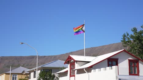 Bandera-Del-Arco-Iris-Del-Orgullo-Del-Progreso-Inclusivo-Intersexual-En-El-Asta-De-La-Bandera-En-El-Edificio-En-Un-Día-Soleado-De-Verano