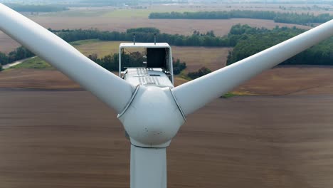 Wind-Turbine-Close-Up-Shot-with-Drone-Ascending-Over-Propellers-and-Tilts-Down-with-Farmland-Fields-in-the-Background