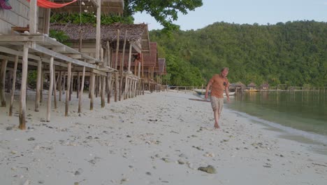 A-man-walks-along-the-sandy-beach-of-Kri-Island-in-the-Raja-Ampat-archipelago,-Indonesia