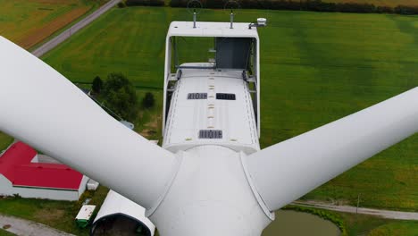 Wind-Turbine-Close-Up-of-Drone-Ascending-Over-the-Propeller-Blades-with-a-Top-Down-View,-Farmland-in-the-Background