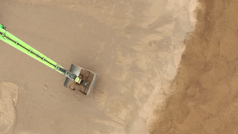 Vista-Aérea-De-Un-Brazo-Verde-Operando-En-Un-Sitio-De-Excavación-Arenoso,-Moviendo-Arena-Con-Precisión