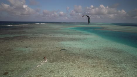 Kiteboarder-glides-over-turquoise-waters-of-a-coral-reef-under-a-partly-cloudy-sky