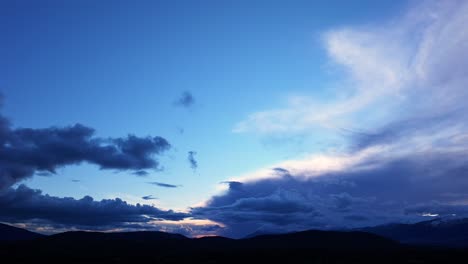 Vuelo-De-Drones-En-Una-Puesta-De-Sol-En-El-Valle-Del-Tiétar-Con-Un-Cielo-Azul-Y-Nubes-Bajas-Corriendo-A-Velocidad-A-Través-Del-Hiperlapso-Sobre-Algunas-Montañas-Oscurecidas-Por-La-Luz-Provincia-De-ávila-España