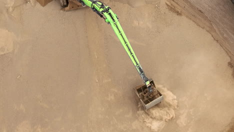 Aerial-view-of-a-green-arm-moving-sand,-creating-a-cloud-of-dust-in-a-sandy-excavation-site